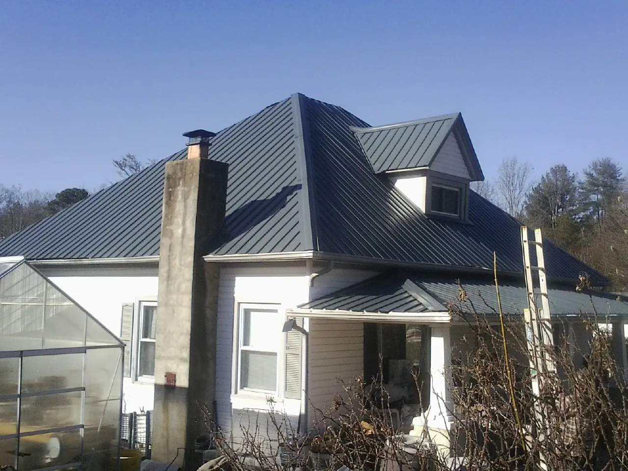 Dark blue standing seam metal roof on a white farmhouse with dormer — Slate & Tile Roof Repair by Roofing Brothers in South Lancaster