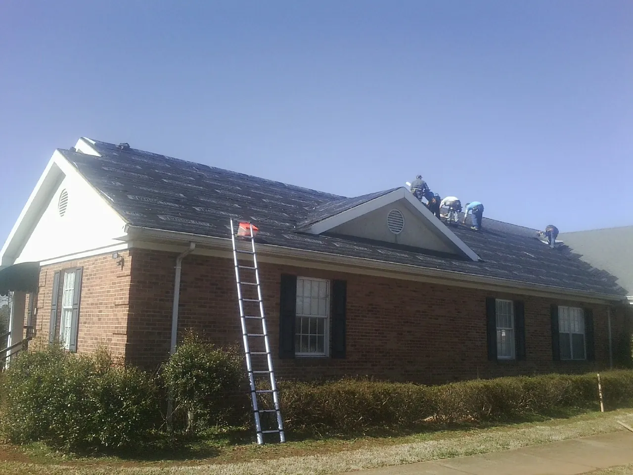 Crew tearing shingles off a brick ranch roof with a ladder set — Metal Roof Repair work by our crew in South Lancaster