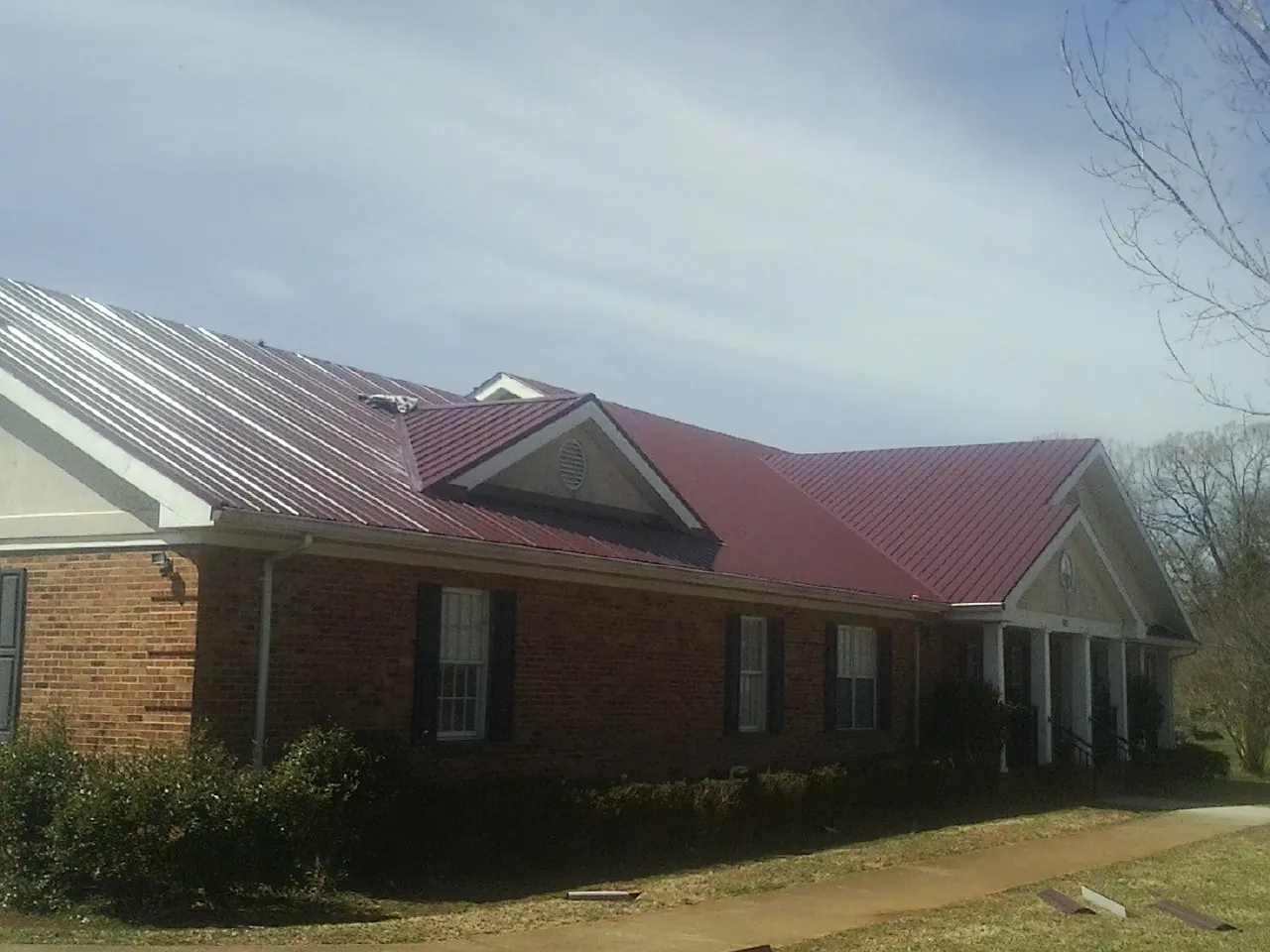 Red metal roof with gabled entries on a long brick building, from a Hail Damage Roof Repair job in South Lancaster