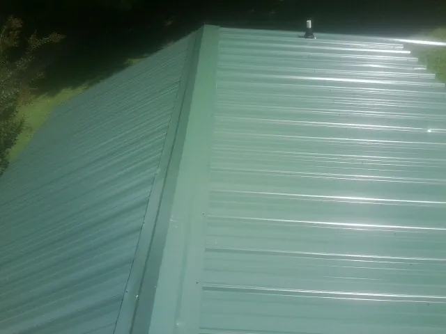 New green metal panels meeting at the ridge of a roof — Flat Roof Repair work by our crew in South Lancaster