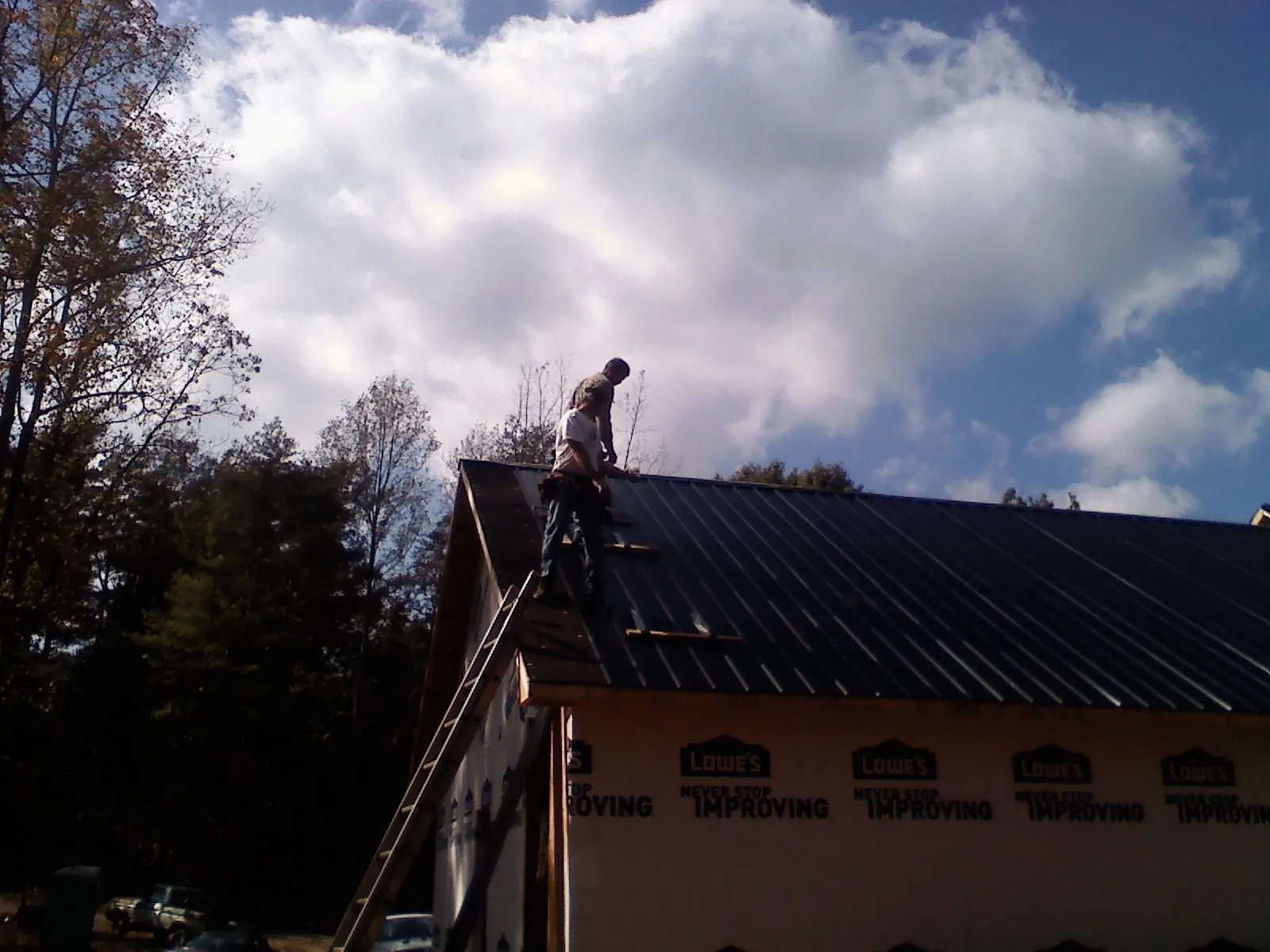 Roofer fastening dark metal panels high against a cloudy sky, from a Roof Inspection job in South Lancaster