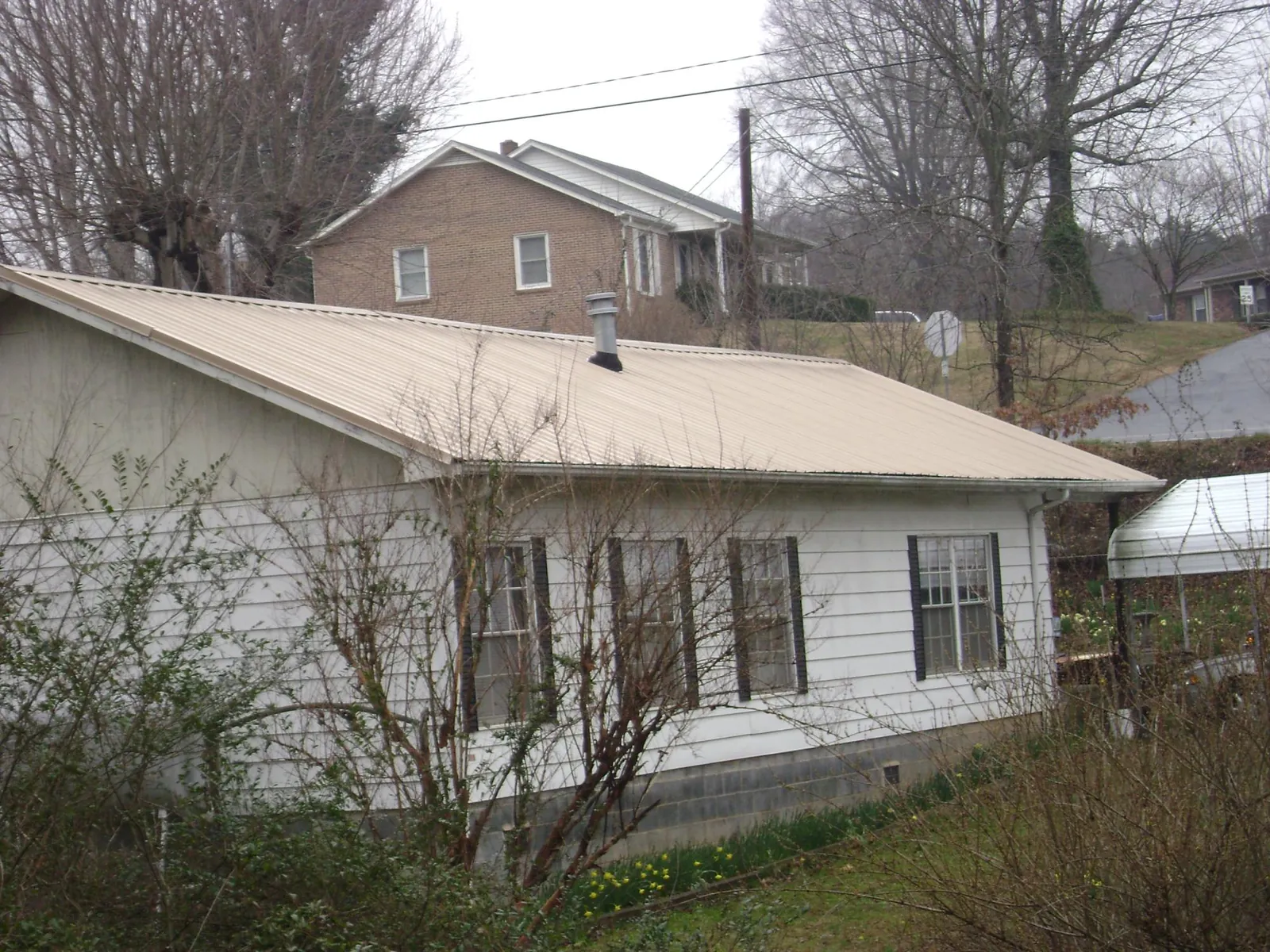 Tan metal roof on a white sided house set into a hillside — Commercial Roofing by Roofing Brothers in South Lancaster
